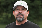 Man wearing a cap and black shirt with a blurred green background