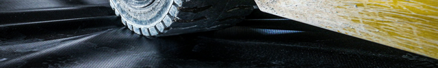 Close-up of a tire on a yellow vehicle with a black tarp underneath.