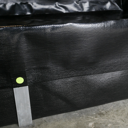 A close-up of a black textured heavy-duty geomembrane secured with silver aluminum L-Brackets on a gray concrete floor.