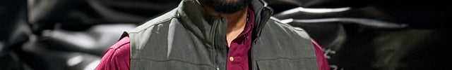 Man wearing a gray vest over a red shirt with a blurred background