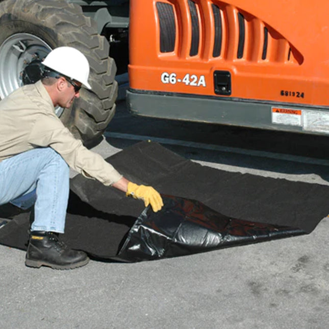 A man bending down to place a black absorbent tarp under a construction vehicle
